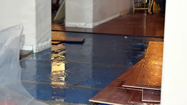 Wet hardwood floorboards being lifted over a plastic sheeted subfloor